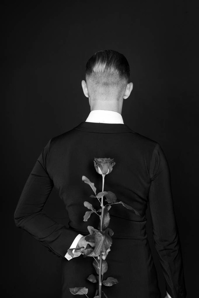 Ballroom dancer with flower on dark background. Man hide rose behind, back view. Valentines day concept. Love, proposal, date. Valentine present, gift, surprise. Holiday celebration, black and white - Photo, Image