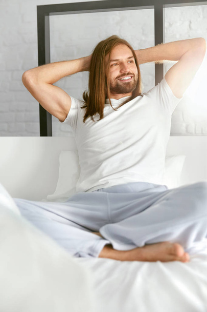 Hombre feliz sentado en la cama en la mañana después de despertar
 - Foto, Imagen