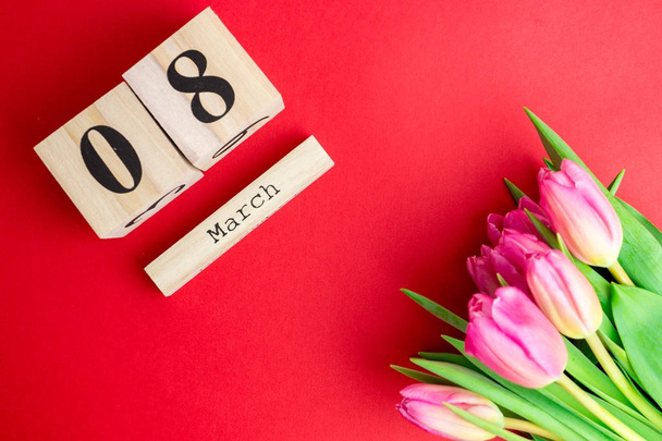 8 Μαρτίου ευτυχισμένη γυναικών μέρα έννοια. Με ξύλινα μπλοκ ημερολόγιο και ροζ τουλίπες σε κόκκινο φόντο - Φωτογραφία, εικόνα