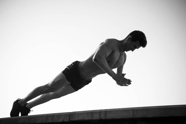 Athlete doing plank exercise on concrete surface. Sportsman exercising on blue sky. Man with ab muscles and fit body. Fitness and sport. Healthy lifestyle concept - Foto, Imagem