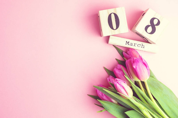 Március 8-i boldog női nap koncepció. A fából készült blokk naptár és rózsaszín tulipánok rózsaszín háttér - Fotó, kép