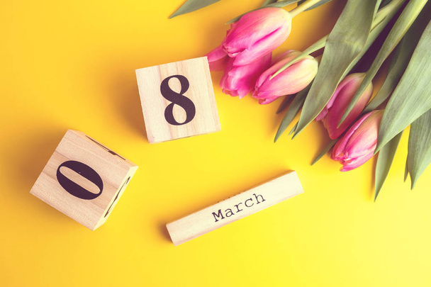 Március 8-i boldog női nap koncepció. A fából készült blokk naptár és rózsaszín tulipán sárga háttérrel. Másolja a hely - Fotó, kép