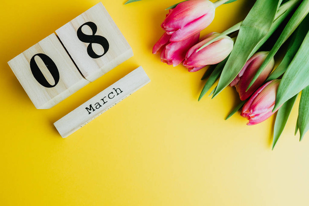 3 月 8 日幸せな女性の日のコンセプトです。黄色の背景に木製のブロック カレンダーとピンク チューリップ。コピー スペース - 写真・画像