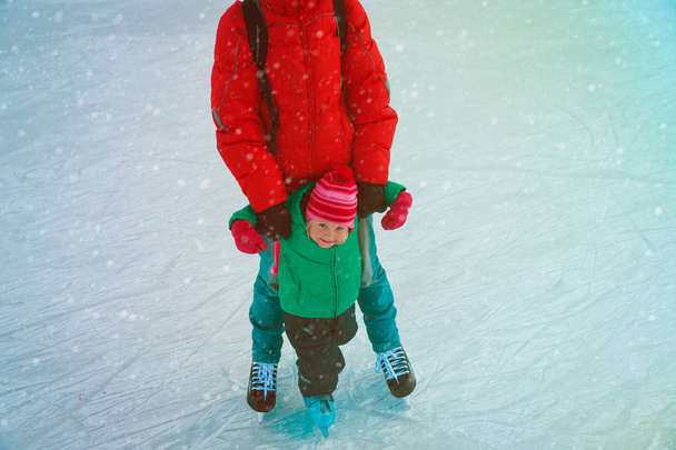 vader en dochtertje leren om te skaten in de winter - Foto, afbeelding