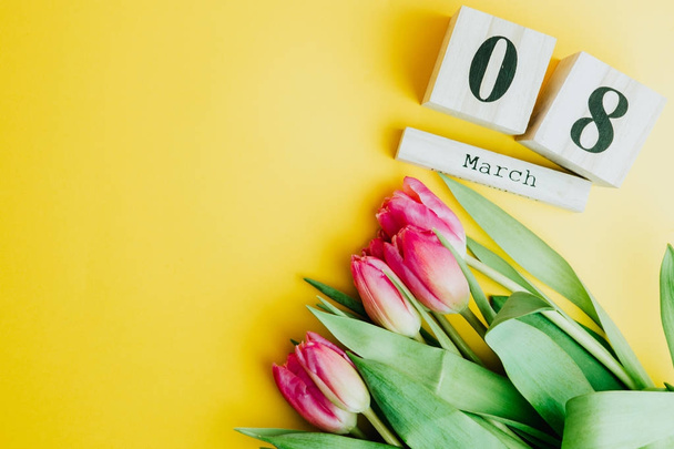 8 maart Happy Women's Day concept. Met houten blok kalender en roze tulpen op gele achtergrond. Kopiëren van ruimte - Foto, afbeelding