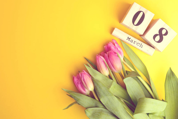 Koncepcja dzień szczęśliwy kobiet 8 marca. Z drewnianym bloku kalendarza i różowe tulipany na żółtym tle. Miejsce - Zdjęcie, obraz