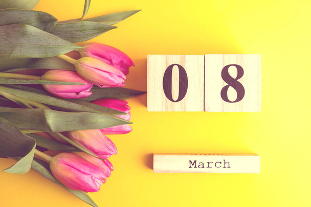 8 de marzo Feliz Día de la Mujer concepto. Con calendario de bloques de madera y tulipanes rosados sobre fondo amarillo. Copiar espacio
 - Foto, Imagen