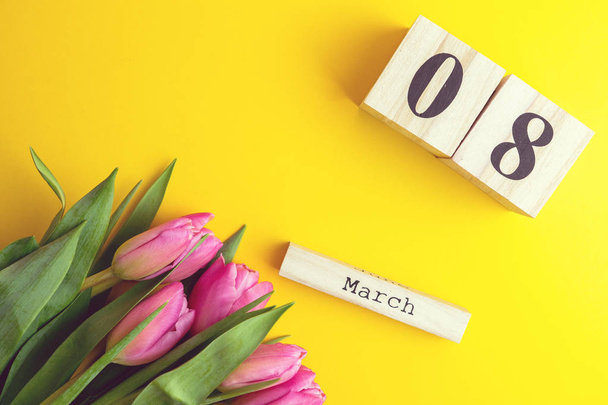 8 de marzo Feliz Día de la Mujer concepto. Con calendario de bloques de madera y tulipanes rosados sobre fondo amarillo. Copiar espacio
 - Foto, imagen