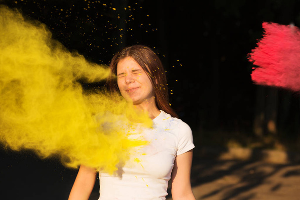 Cheerful young model with exploding yellow and pink  powder cele - Foto, immagini