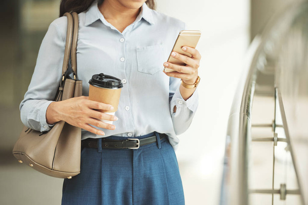 Copped imagem de mulher de negócios com xícara de café verificando seu smartphone
 - Foto, Imagem