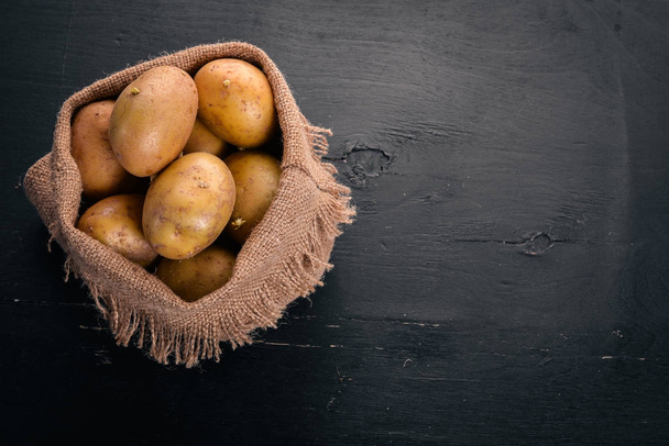 Raw potatoes on a black wooden background. Cooking. Free space for text. Top view. - Foto, Imagen