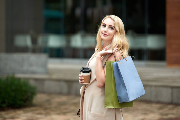 Porträt einer schönen jungen blonden Frau, die mit Einkaufstüten im Freien posiert und in die Kamera lächelt - Foto, Bild