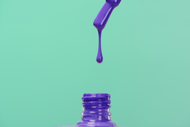 nagel Pools gieten neer in fles geïsoleerd op turquoise - Foto, afbeelding