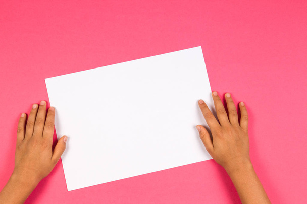 Handen van de kinderen met witte blanco papier kaart op roze achtergrond - Foto, afbeelding