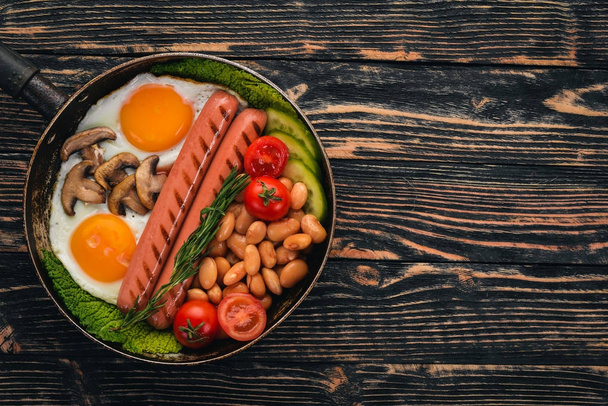 English breakfast - fried egg, beans, tomatoes, mushrooms, bacon and toast. Top view. On a wooden background. - Fotoğraf, Görsel