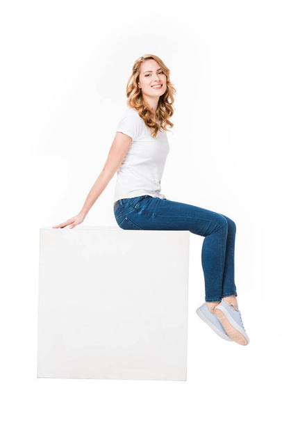 cheerful woman sitting on empty  white cube isolated on white - Photo, image