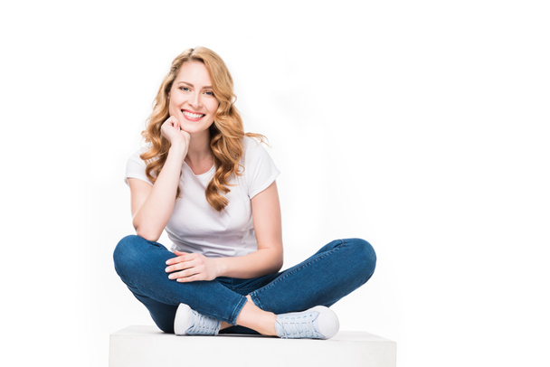 smiling woman sitting on white cube isolated on white - Foto, immagini