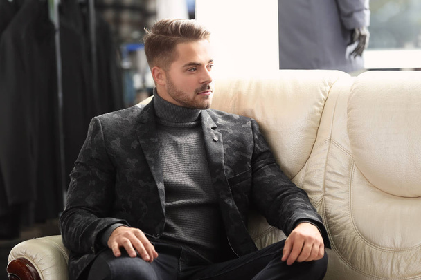 Young man in stylish clothes sitting on sofa at menswear store - Fotografie, Obrázek