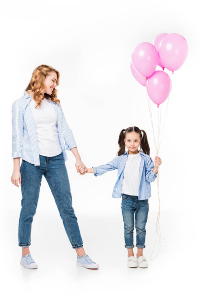 moeder en dochter glimlachend met roze ballonnen hand in hand geïsoleerd op wit - Foto, afbeelding