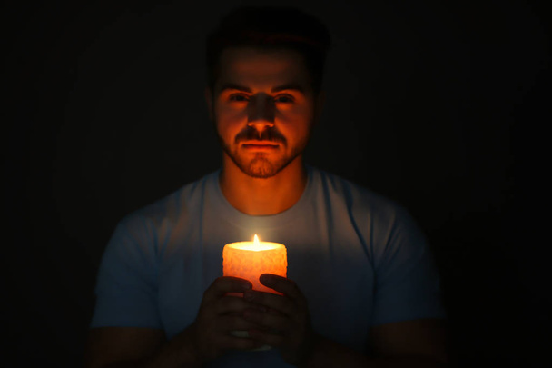Handsome young man with burning candle in darkness - Foto, Bild