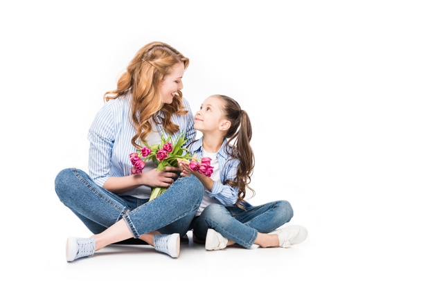 happy mother and little daughter with bouquet of flowers looking at each other isolated on white, mothers day concept - Foto, Imagem
