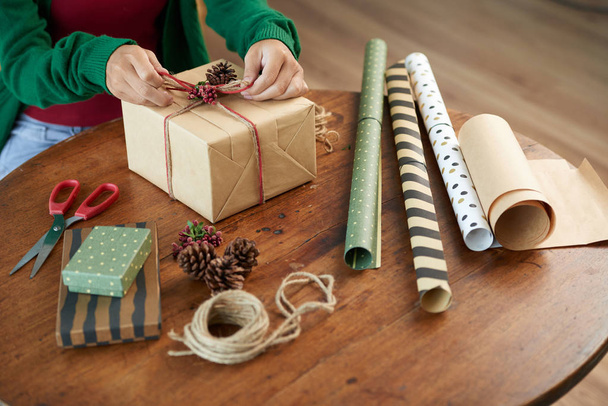 Femme créative utilisant du papier artisanal, des baies et des cônes lors de l'emballage présent
 - Photo, image