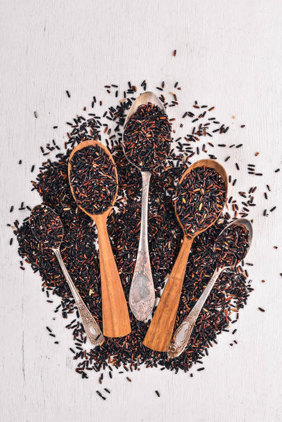 Black wild dry rice on a spoon. On a wooden background. Top view. Copy space. - Photo, image
