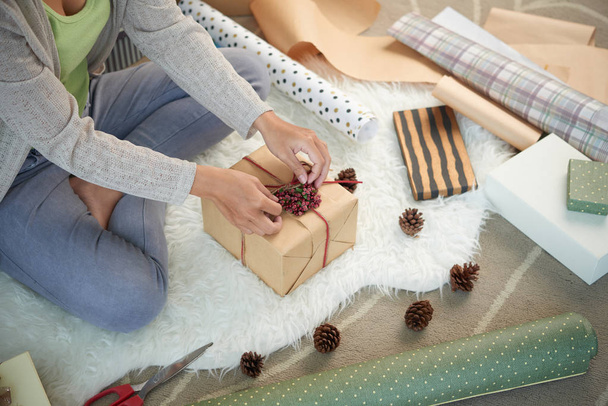 Mujer que usa bayas y conos de pino al decorar la caja de regalo
 - Foto, Imagen