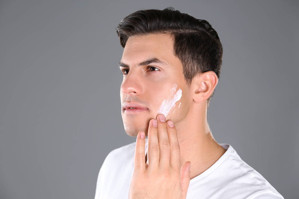 Handsome man applying face cream on grey background - Foto, afbeelding