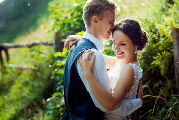 Retrato emocional de la hermosa pareja recién casada con una sonrisa encantadora abrazándose tiernamente en el soleado jardín verde
. - Foto, imagen