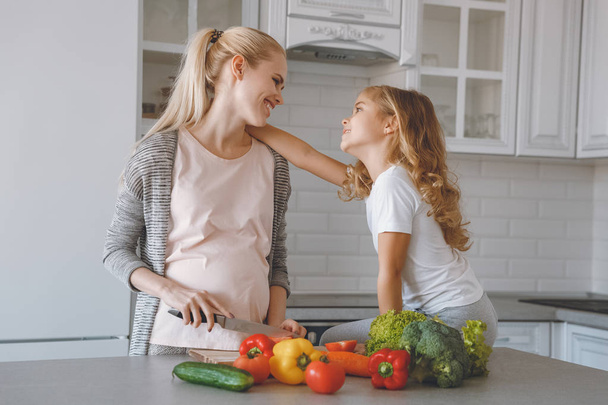 Tochter umarmt schwangere Mutter beim Kochen in der Küche - Foto, Bild