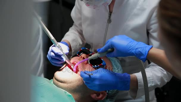 Dentysta i pielęgniarka naprawy zębów pacjenta człowieka. Użycie bormashenko do wiercenia zęby i usuwanie próchnicy zębów i uszczelnienie - Materiał filmowy, wideo