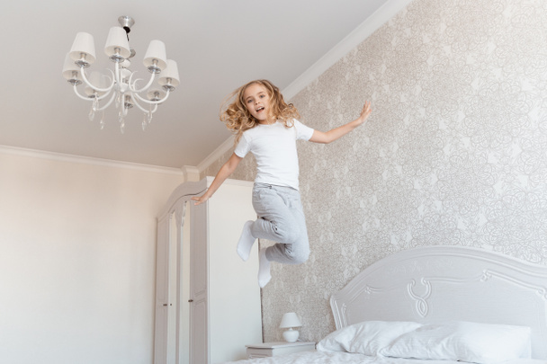 smiling child jumping on bed and looking at camera - Foto, Bild