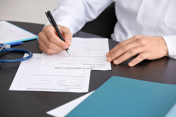 Doctor filling in insurance form at table - Φωτογραφία, εικόνα