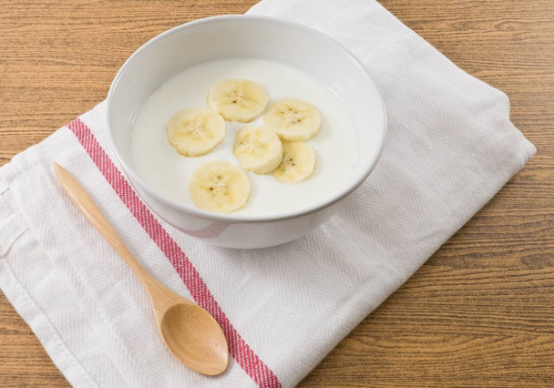タンパク質、カルシウム、リボフラビン、ビタミン B6、ビタミン B12 の栄養豊富な熟したバナナをのせた自家製ヨーグルトのボウル. - 写真・画像