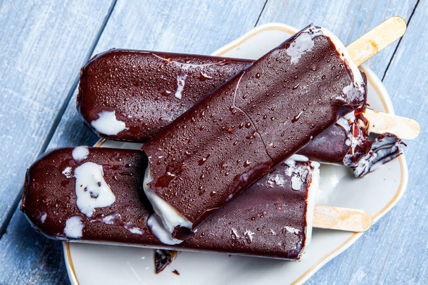 Crème glacée au chocolat apparaît sur un fond en bois bleu. Glace au chocolat sur fond rouillé. Crème glacée esquimau sur bâton
. - Photo, image