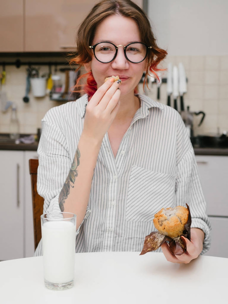 Young smile girl eats muffin on the kitchen - Photo, Image