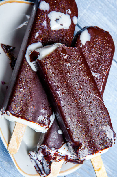 Шоколадное мороженое на голубом деревянном фоне. Шоколадное мороженое на ржавом фоне. Эскимосское мороженое на палочке
. - Фото, изображение