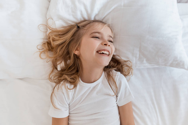 top view of smiling adorable child lying on bed - Foto, afbeelding