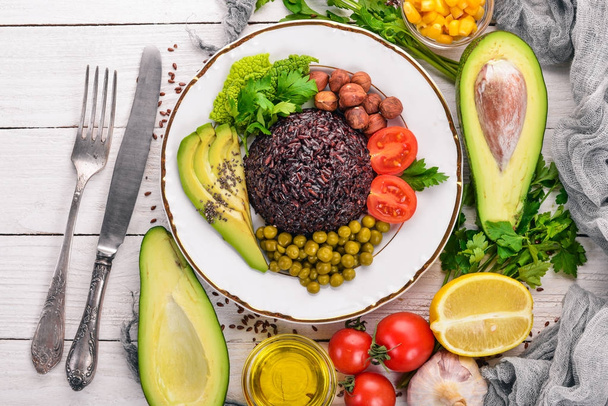 Healthy food. Black rice, avocado, cherry tomatoes, green peas and hazelnut. On a wooden background. Top view. Free space for your text. - Photo, Image