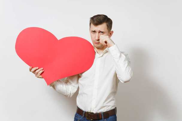 Sad upset crying man in shirt holding big red heart isolated on white background. Copy space, advertisement. Place for text. St. Valentine's Day, International Women's Day, birthday, holiday concept. - Fotografie, Obrázek