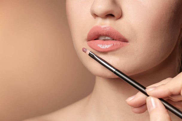 Professional visage artist applying makeup on woman's face on color background - Foto, Imagen