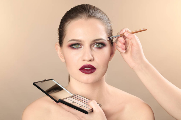 Professional visage artist applying makeup on woman's face on color background - Foto, imagen