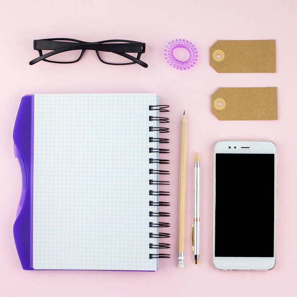Creative flat lay photo of workspace desk with smartphone, eyeglasses, pen, pencil and notebook, minimal style on pink background. Minimal business concept - Photo, Image