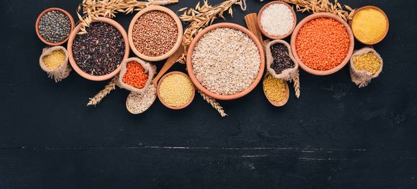 Set of Groats and Grains. Buckwheat, lentils, rice, millet, barley, corn, black rice. On a black background. Top view. Copy space. - 写真・画像