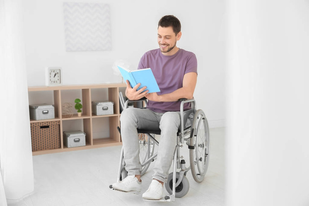 Young man in wheelchair reading book indoors - Foto, Imagem