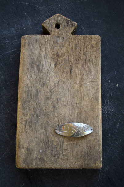 Still life with old  kitchen cutting board and metal spoon-bait fish   - Photo, Image