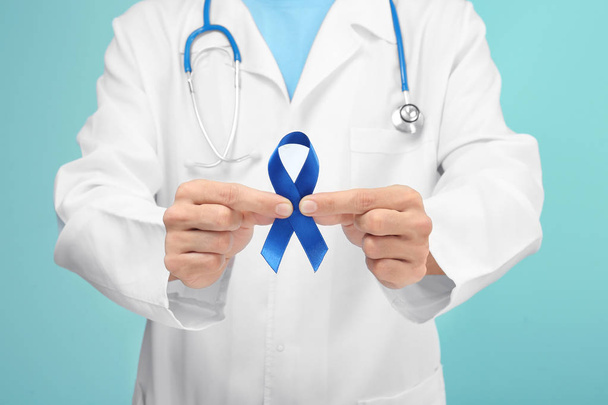 Doctor holding blue ribbon on color background, closeup. Prostate cancer awareness - Фото, зображення
