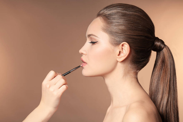 Professional visage artist applying makeup on woman's face on color background - Fotografie, Obrázek