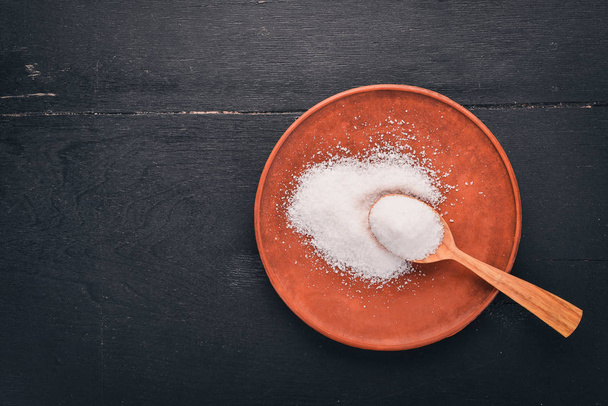 Salt in a wooden spoon on a plate. On a wooden background. Top view. Free space for text. - 写真・画像